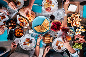 Above aerial view of group of friends having fun eating together at lunch or dinner with a table full of different and colorful food and technology mobile phone. mix of hands of caucasian people taking somethings to eat together
