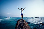 Freedom young woman outstretched arms on seaside rock cliff edge