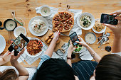 Group of friends taking pictures of food on the table with smartphones during party