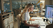 Night, business woman and graphic designer on computer in office at table working on deadline. Creative, serious and professional at desk, editing software and retouching project online in startup.