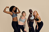 Happy fit diverse young women group having fun at beige background.