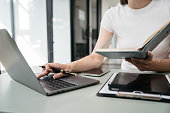 Female businessman use a smartphone and take notes in the notebook at the office desk in the morning.