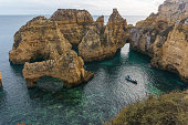Famous rock formation of cliff at the atlantic coast line near Ponta da Piedade with boat in bay of clear blue water, Lagos, Algarve, Portugal.