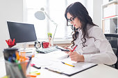 A young girl is sitting at the office desk, working with a calculator and documents.