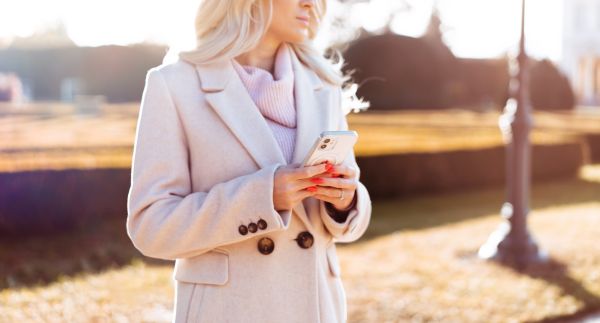 Woman in Coat Holding Her White Smartphone in Hands During Sunny Fall Free Stock Photo